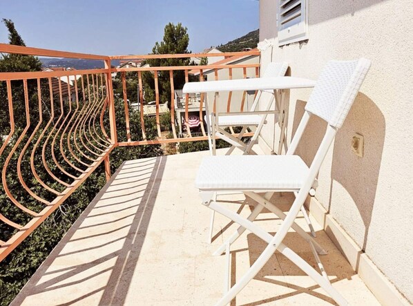 A balcony with a white lounge chair, a small table, and a metal railing.