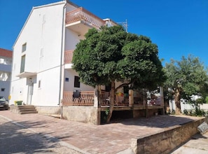 A two-story building with a balcony, a tree in front, and a paved area.