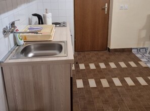 A kitchen with a sink, a wooden cabinet, a tiled floor, and a door.