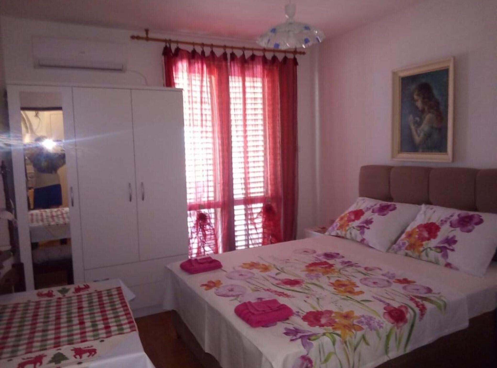 A bedroom with a bed, a wardrobe, and a window with red curtains.