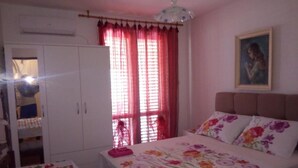 Een slaapkamer met een bed, een kledingkast en een raam met rode gordijnen.