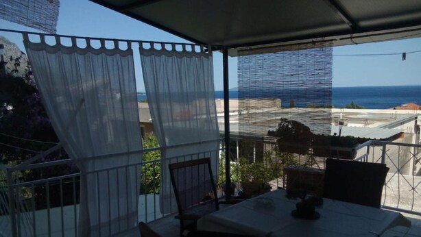 Een overdekt terras met een tafel en stoelen, met uitzicht op de kust.