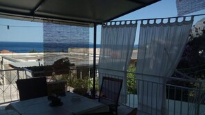 Een overdekt terras met een tafel en stoelen, met uitzicht op zee.