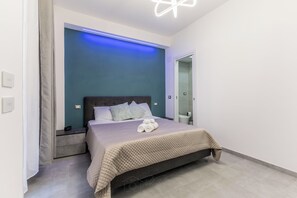 A modern bedroom with a bed, a nightstand, a mirror, and a blue accent wall. - gordiani guesthouse (Rome)