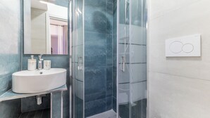 Une salle de bain moderne avec une douche à parois de verre, un lavabo blanc avec un miroir et un luminaire fixé au mur.