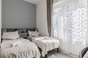 A hotel room with two beds, a grey headboard, and a window with patterned curtains. - gordiani guesthouse (Rome)