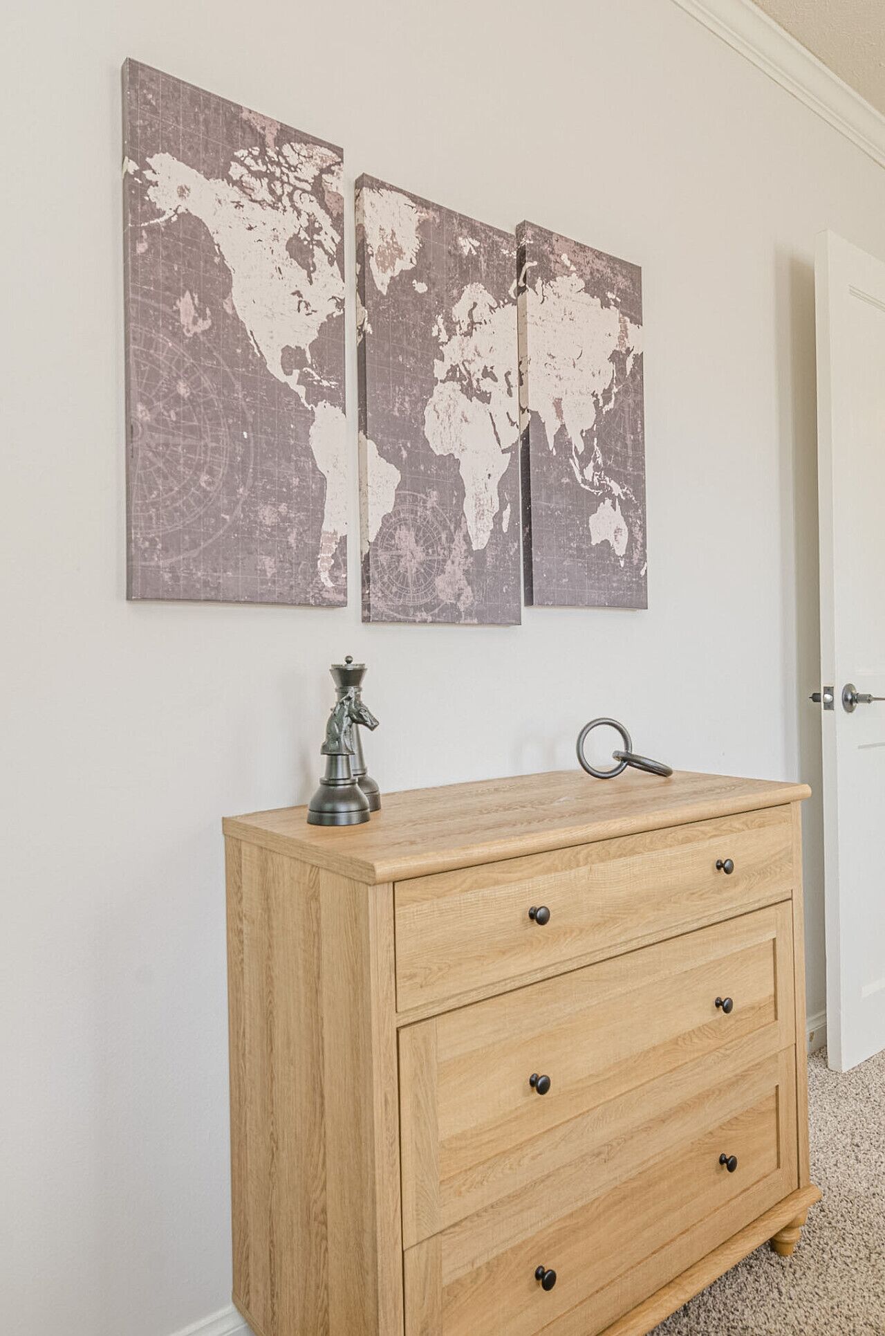 A wooden cabinet with drawers and a globe ornament on top, against a white wall with two world map paintings.