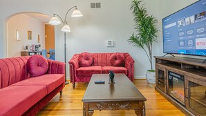 A living room with two red sofas, a wooden coffee table, a floor lamp, a television, and a potted plant. - MidTown Flats Suite C2 (Columbus)