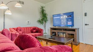 A living room with a red velvet sofa, a wooden coffee table, and a flat-screen TV on a wooden stand. - MidTown Flats Suite C2 (Columbus)