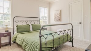 A bedroom with a metal bed frame, green bedding, a bedside table with a lamp, and a door. - MidTown Flats Suite C2 (Columbus)