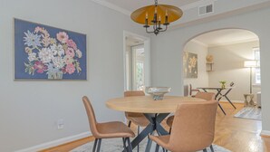 A dining area with a round table, four chairs, a chandelier, and a floral painting on the wall. - MidTown Flats Suite C1 (Columbus)