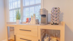 A wooden cabinet with a coffee maker, a stack of coffee pods, and a plant on top. - MidTown Flats Suite C1 (Columbus)