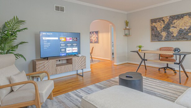 A modern living room with a flat-screen TV, comfortable seating, a dining area, and a hallway leading to another room. - MidTown Flats Suite C1 (Columbus)