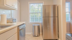 A kitchen with a stainless steel refrigerator, a sink, a dishwasher, and a window with blinds. - MidTown Flats Suite C1 (Columbus)