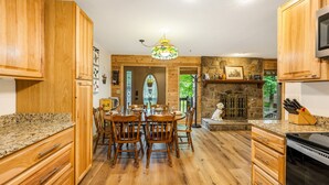 A kitchen with wooden cabinets, granite countertops, a dining table with chairs, and a stone fireplace.
