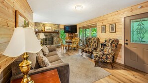 A cozy living room with wooden walls, a fireplace, a television, and a dining area with chairs and a table.
