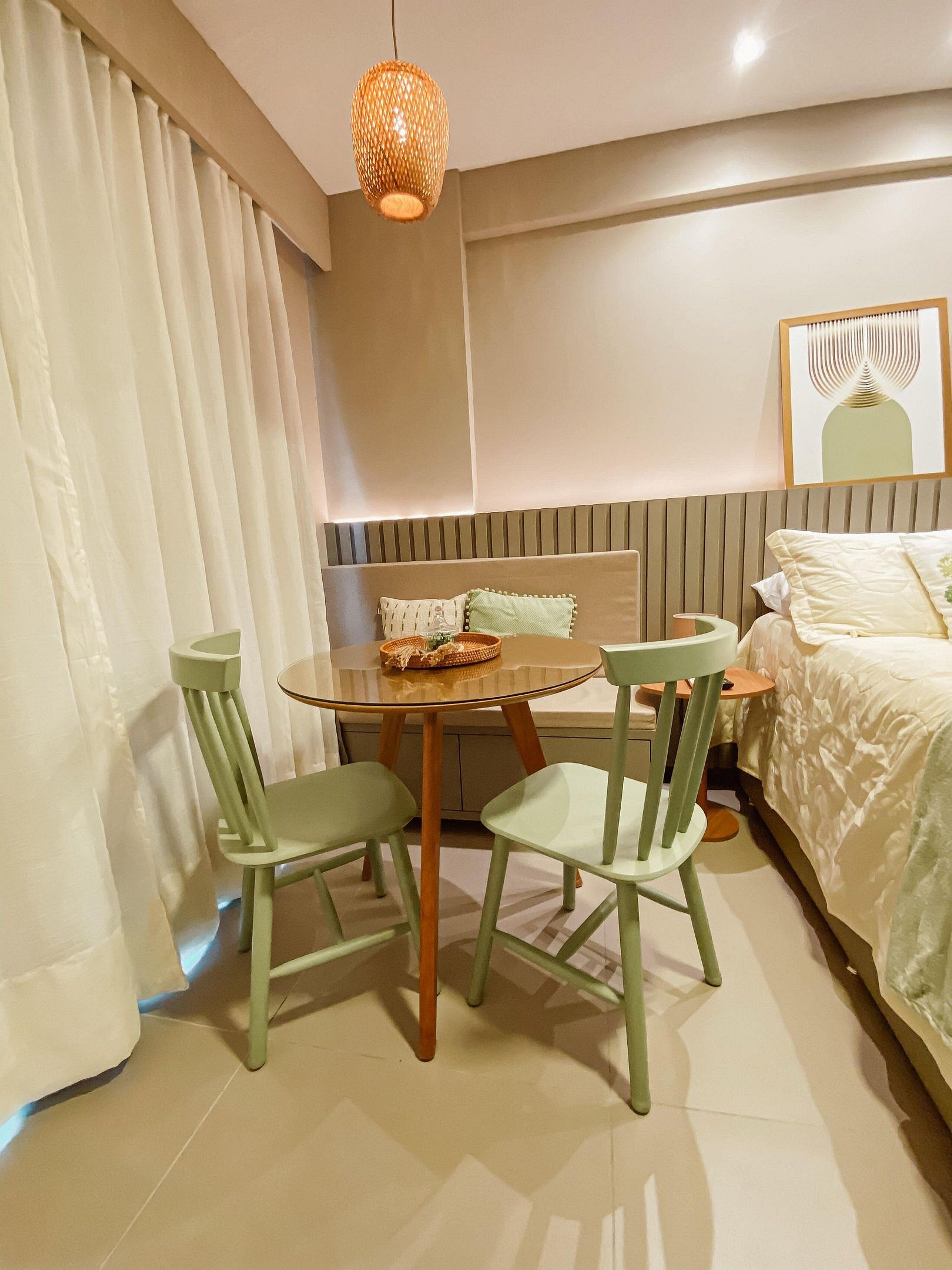 Habitación de hotel con cama, una mesa redonda con sillas, una lámpara colgante y un cuadro en la pared.