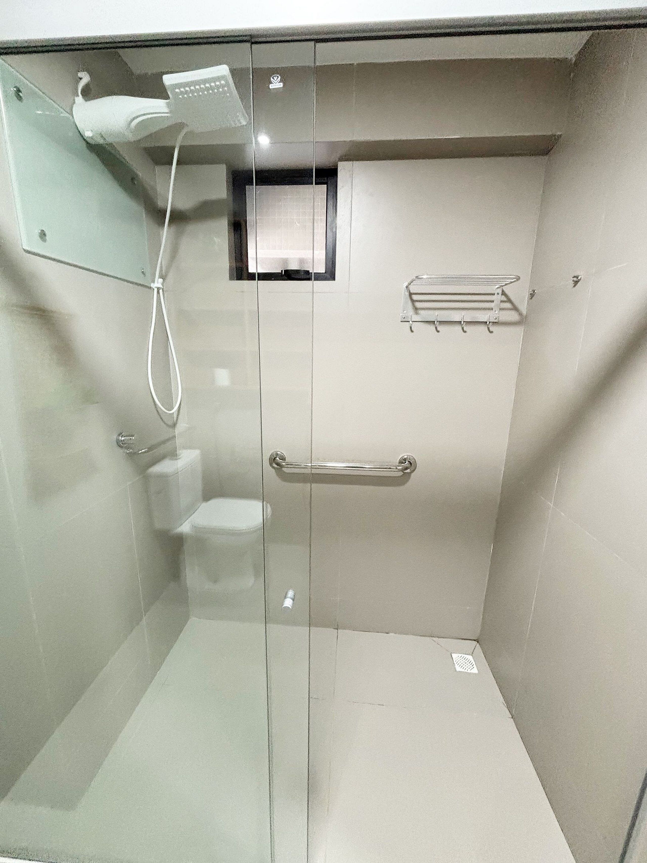 Een kleine, afgesloten douchecel met een glazen deur, een handdouche, toilet en een handdoekhouder.