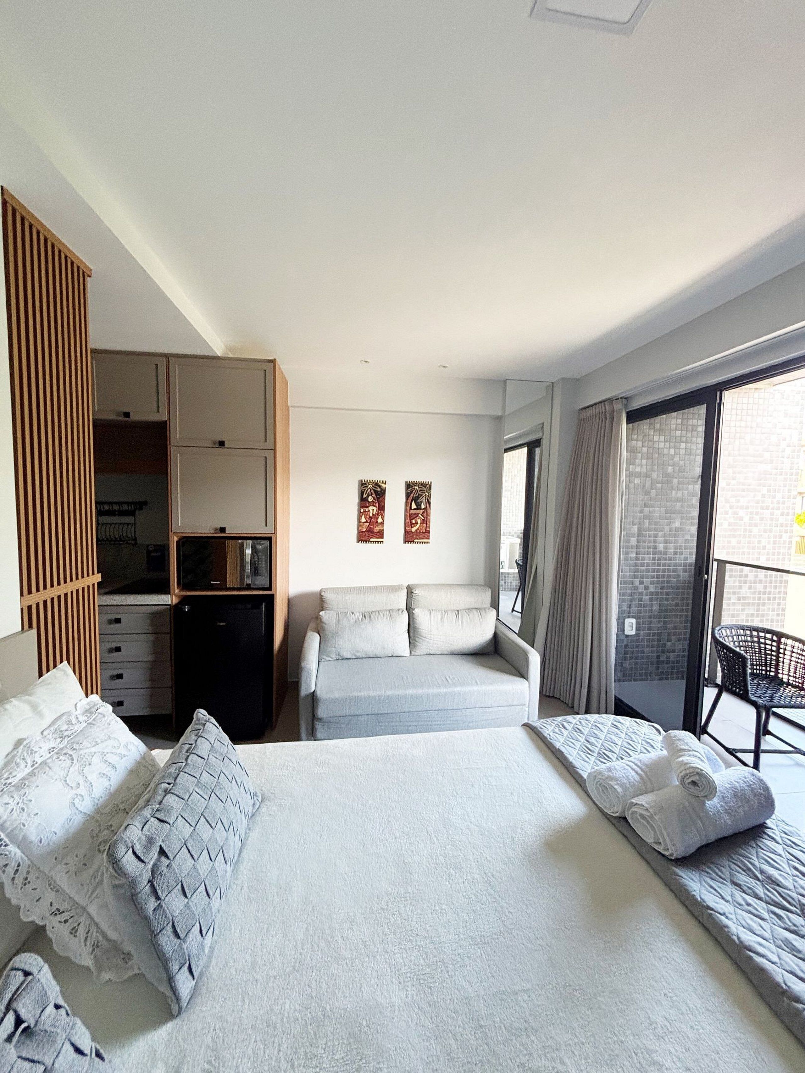 Una habitación de hotel con cama, sofá, armario, una mesita y un balcón con una silla.