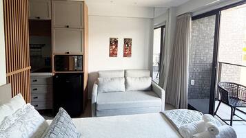 Una habitación de hotel con cama, sofá, armario, una mesita y un balcón con una silla.