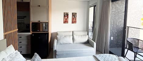 A hotel room with a bed, a sofa, a wardrobe, a small table, and a balcony with a chair.