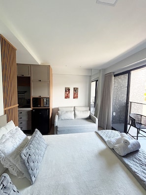Una habitación de hotel con cama, sofá, armario, una mesita y un balcón con una silla.