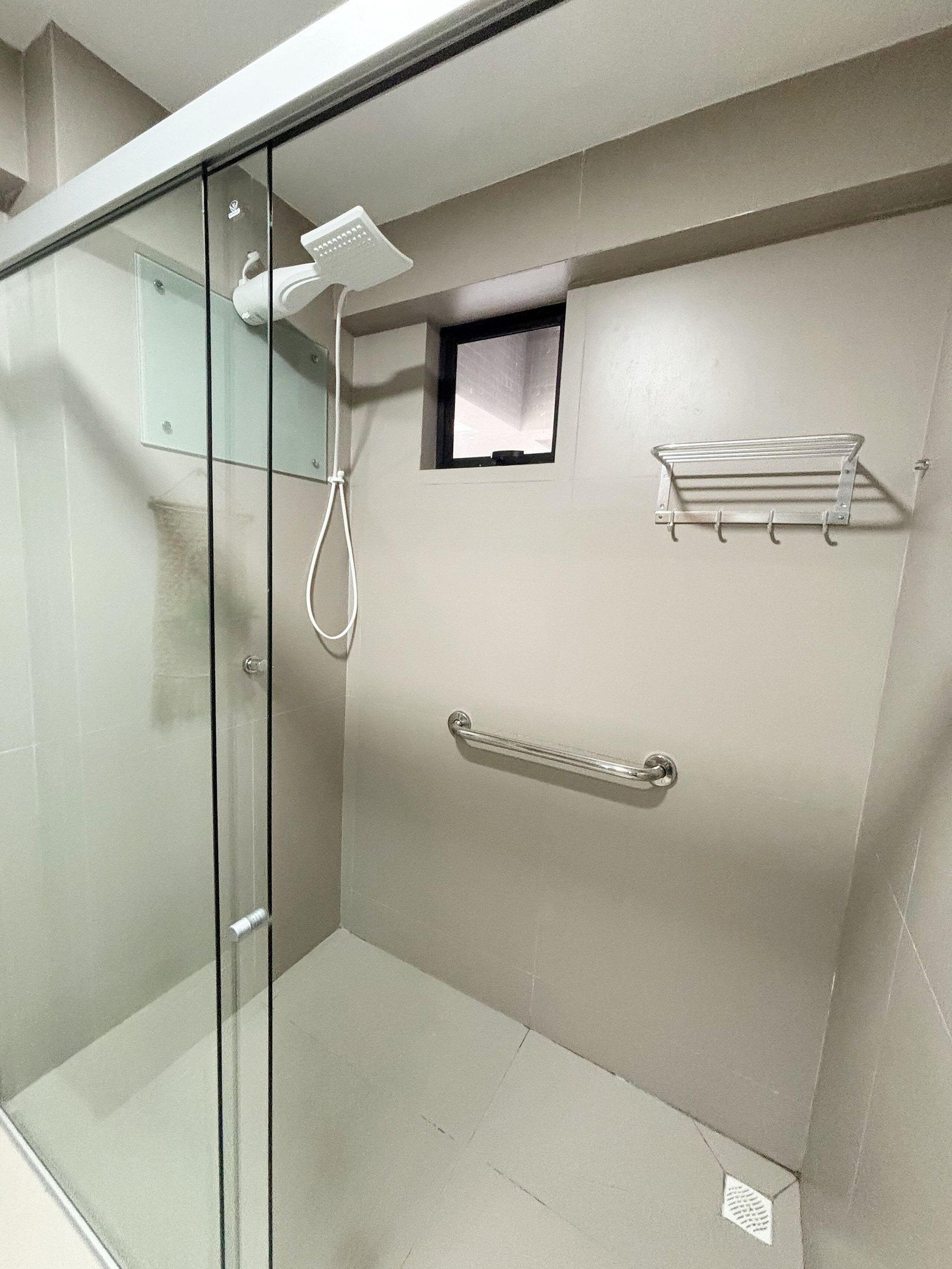 Ducha con cerramiento de vidrio, un cabezal de ducha manual, un perchero y un ventanal pequeño.
