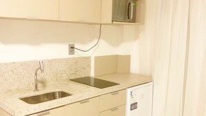 A compact kitchen with a built-in microwave, a sink, and a small refrigerator. - Beach Haus by Day by Day (Joao Pessoa)