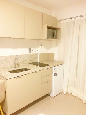 Cocina compacta con microondas integrado, lavamanos y un refrigerador pequeño.