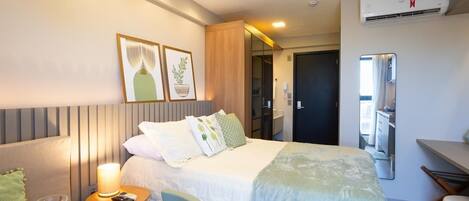 A hotel room with a bed, bedside table, lamp, and a mirror.