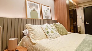 A hotel room with a bed, bedside table, lamp, remote control, and framed artwork on the wall. - Beach Haus by Day by Day (Joao Pessoa)