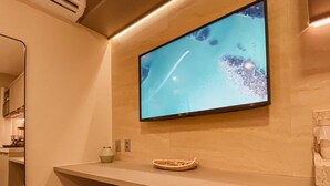 A modern bathroom with a mounted TV, a mirror, and two stools. - Beach Haus by Day by Day (Joao Pessoa)