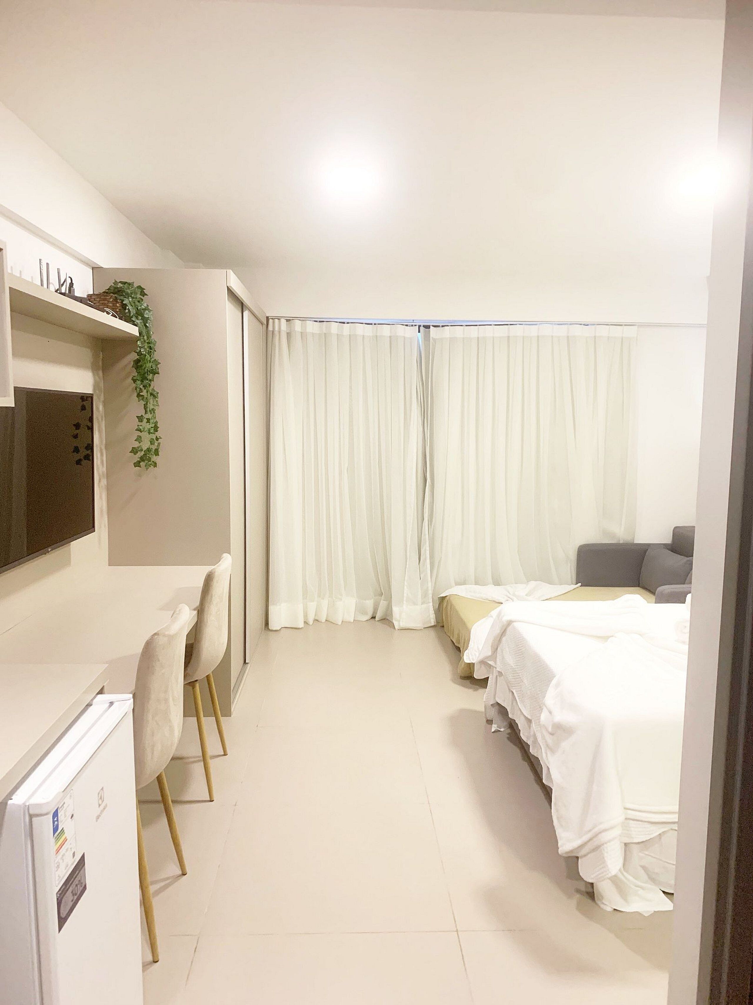 Ein Hotelzimmer mit Bett, Schreibtisch, Stuhl, Fernseher und einem fensterbepflanzten Fenster.