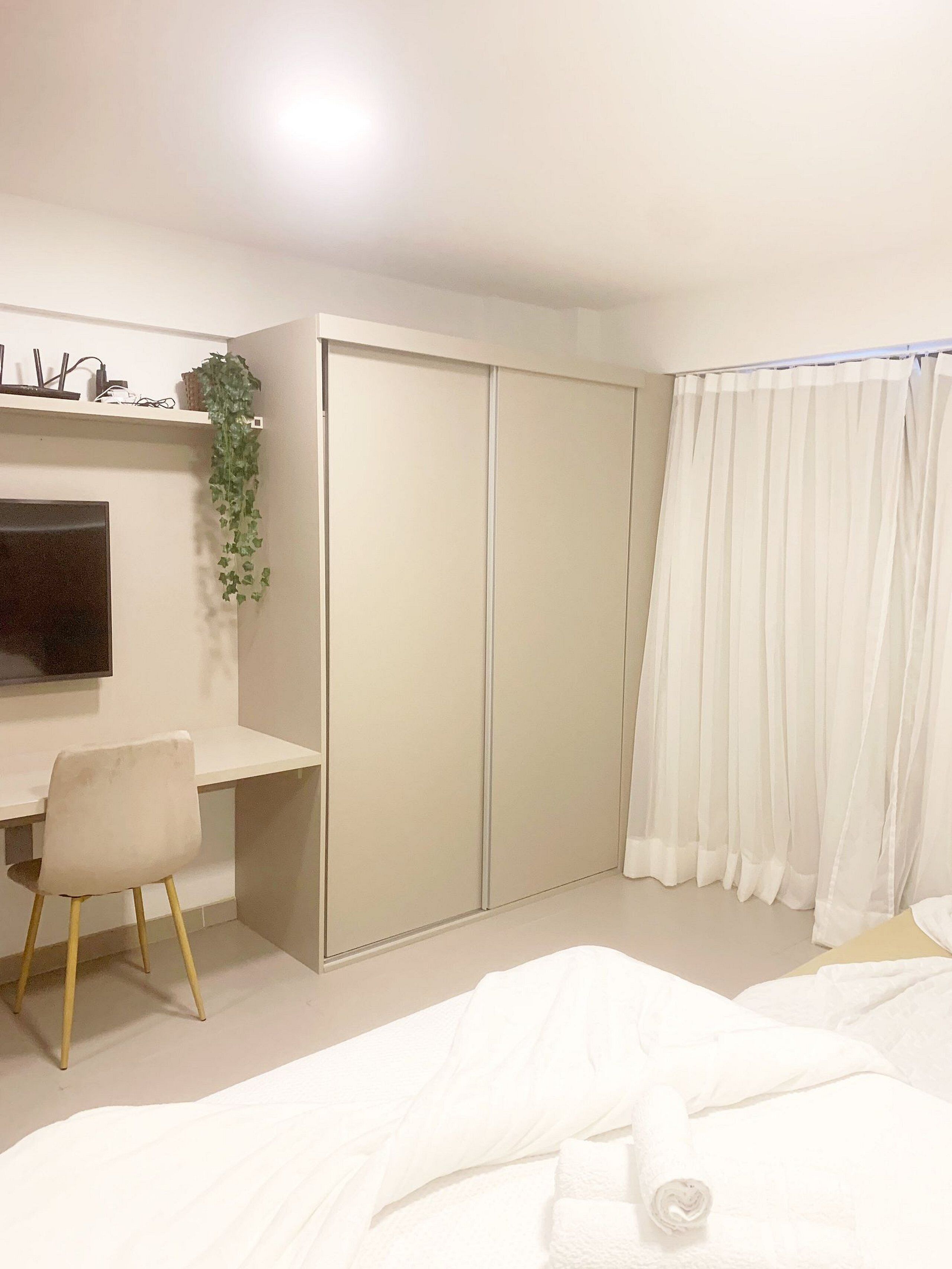 A bedroom with a bed, a desk, a chair, a wardrobe, and a window with curtains.
