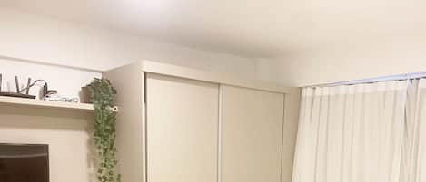 A bedroom with a bed, a desk, a chair, a wardrobe, and a window with curtains.