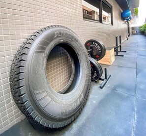 A tire mounted on a wall, a set of weights, and a wooden box on a sidewalk. - Beach Haus by Day by Day (Joao Pessoa)