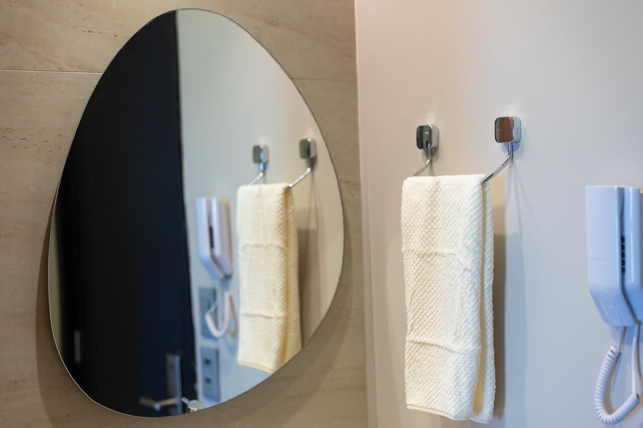 Un bagno con un grande specchio ovale, due asciugamani bianchi appesi a ganci e un telefono bianco fissato alla parete.