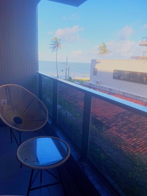 A balcony with wicker chairs, a view of the sea, and a building with a white facade. - Beach Haus by Day by Day (Joao Pessoa)