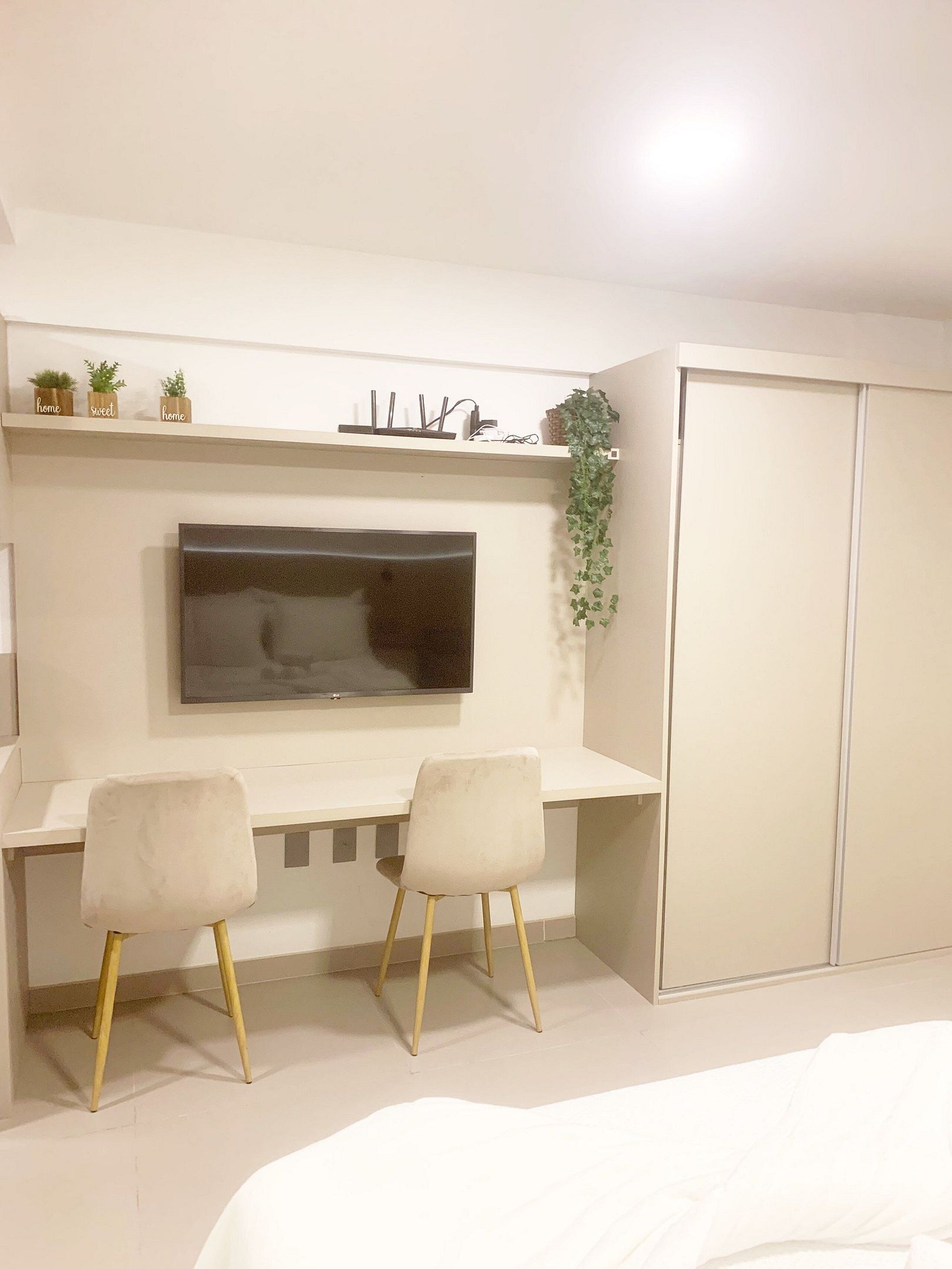 Ein Schlafzimmer mit Bett, Schreibtisch mit zwei Stühlen, Fernseher, Kleiderschrank und Regal mit Pflanzen und Dekoration.