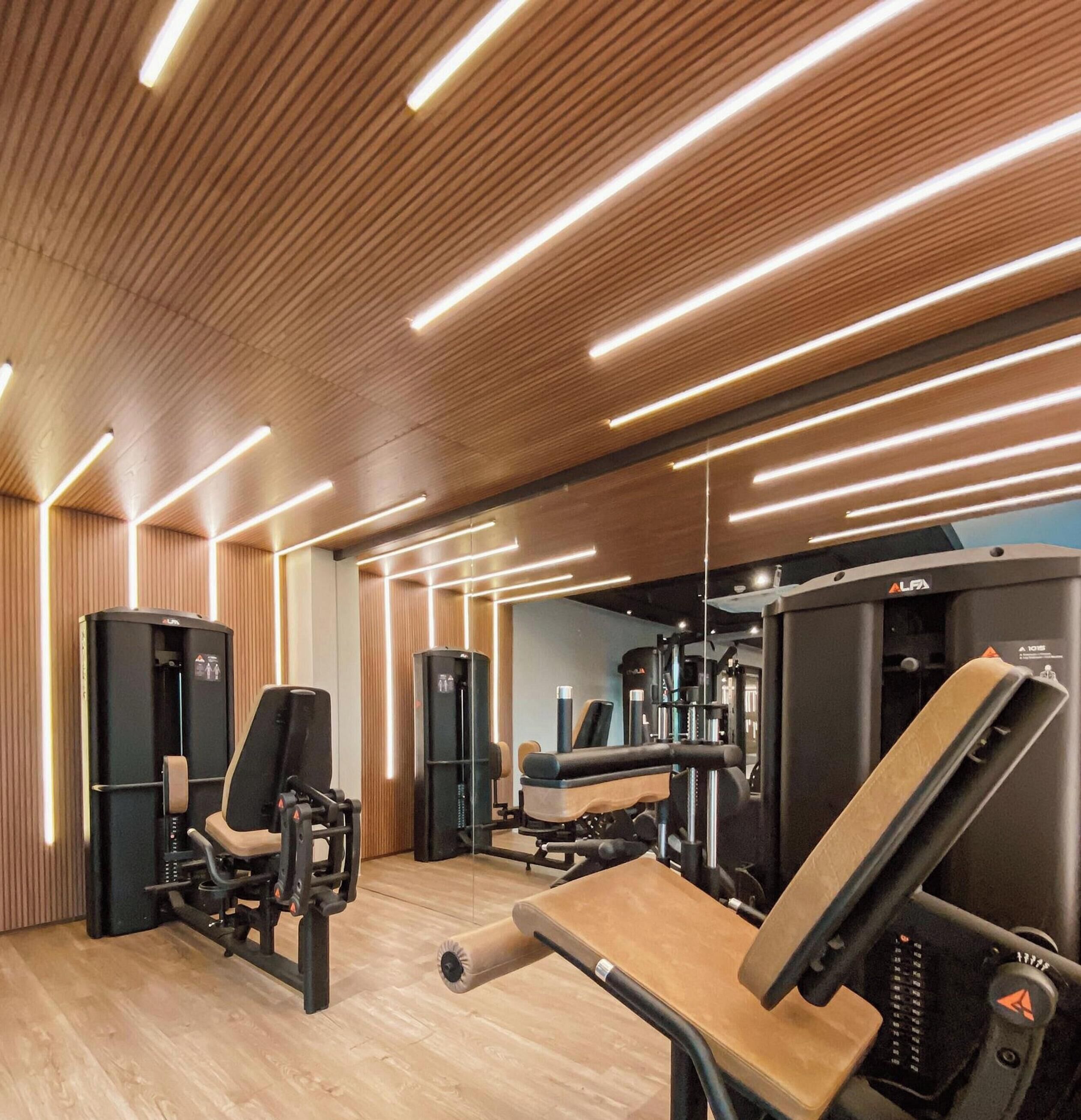 Un gimnasio con equipo de ejercicio, paredes de paneles de madera e iluminación moderna.