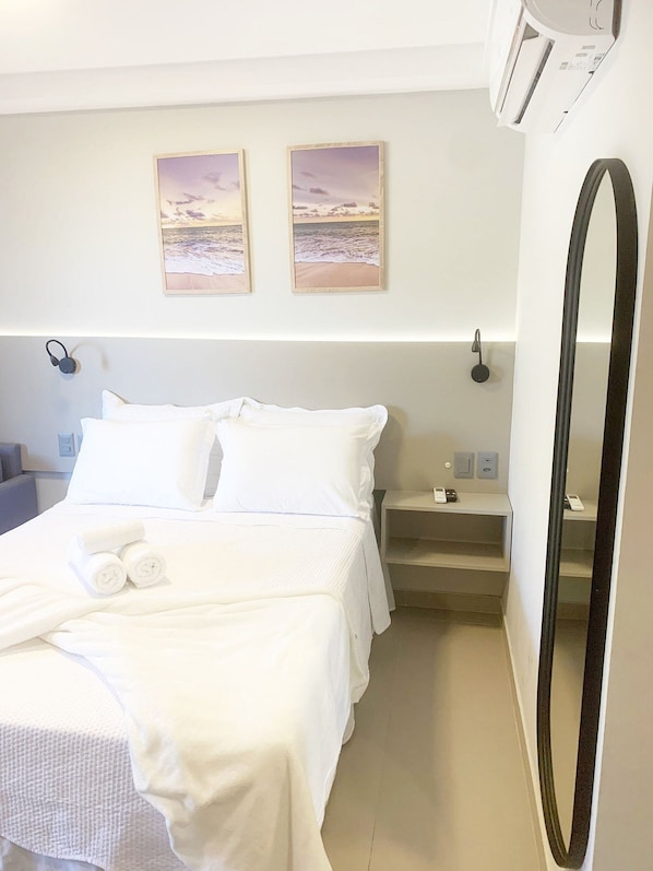Una habitación de hotel con una cama, dos cuadros en la pared, una mesita de noche con un teléfono y un espejo grande.