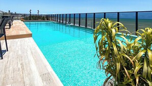Una piscina con vistas al océano, rodeada por una terraza y plantas en macetas.