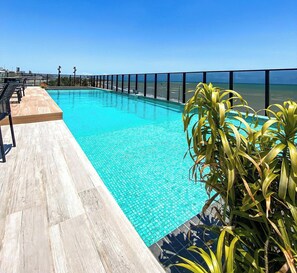A swimming pool with a view of the ocean, surrounded by a deck and potted plants. - Beach Haus by Day by Day (Joao Pessoa)