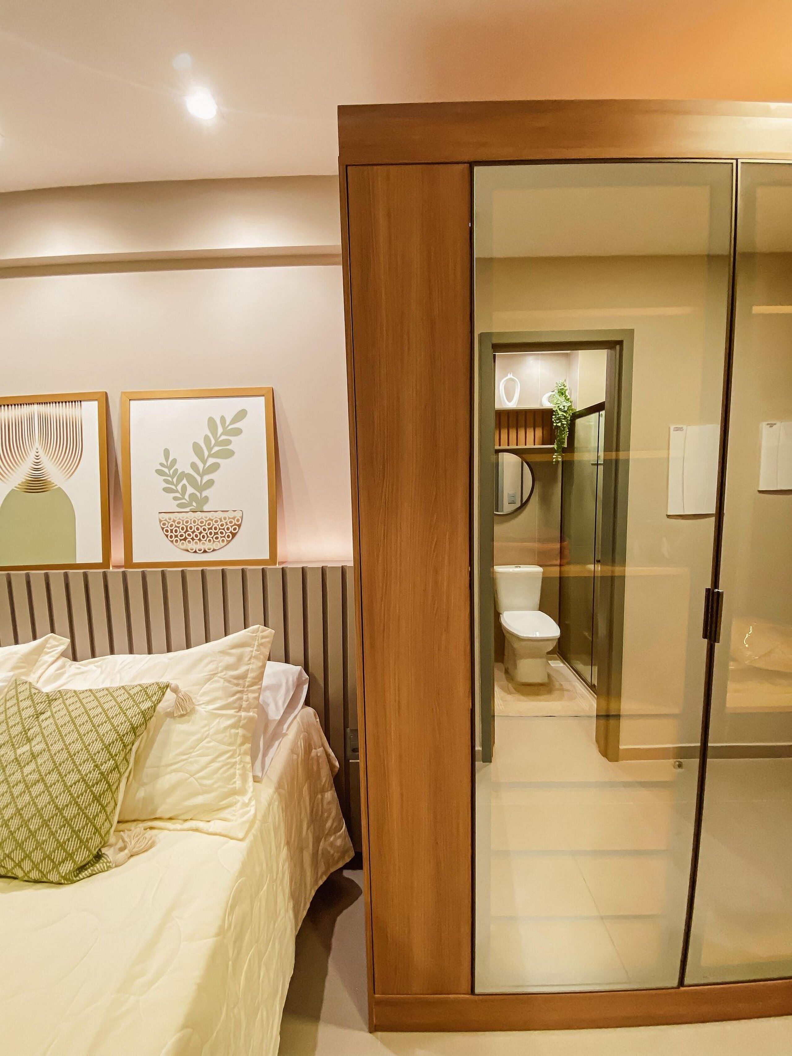 Une chambre à coucher avec un lit, une armoire en bois et une salle de bain visible à travers une porte en verre.