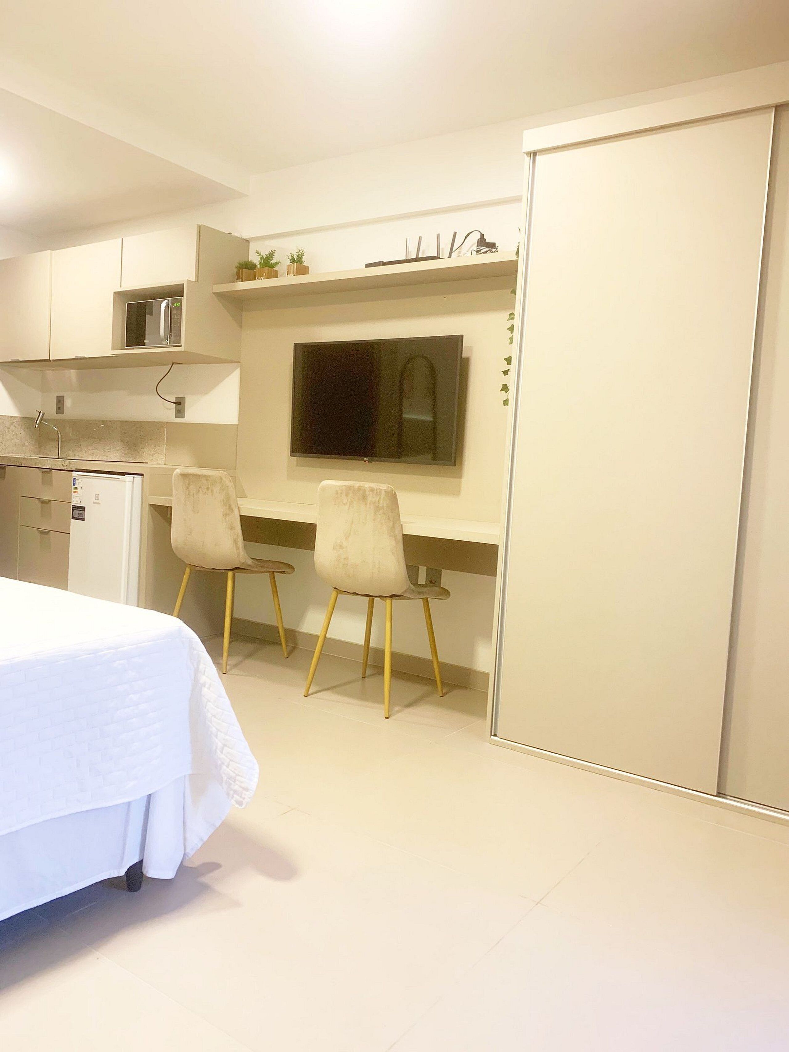 Una habitación compacta con cama, kitchenette, dos sillas, televisor y puerta corredera.