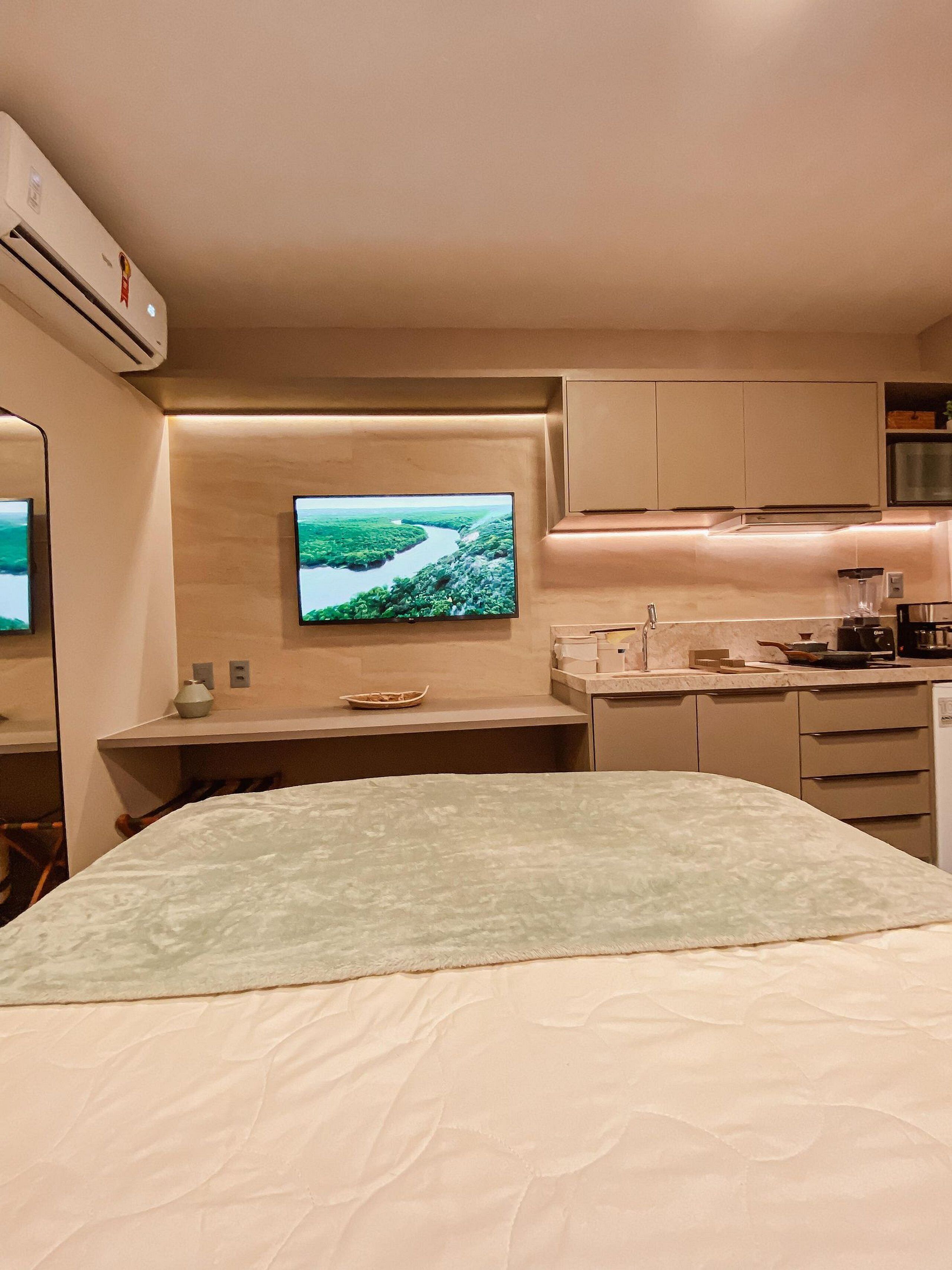 Une chambre compacte comprenant un lit, un téléviseur fixé au mur, une petite kitchenette et une fenêtre donnant sur une rivière.
