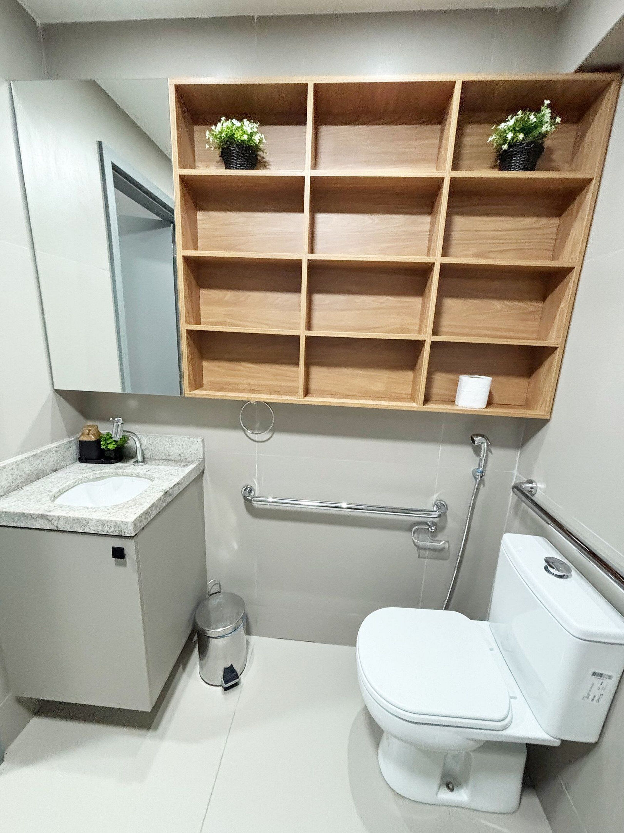 A bathroom with a white sink, toilet, and a wooden shelf above the toilet.