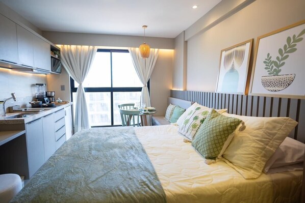 Quarto de hotel moderno com cama, uma pequena escrivaninha, uma cadeira e janela com cortinas.