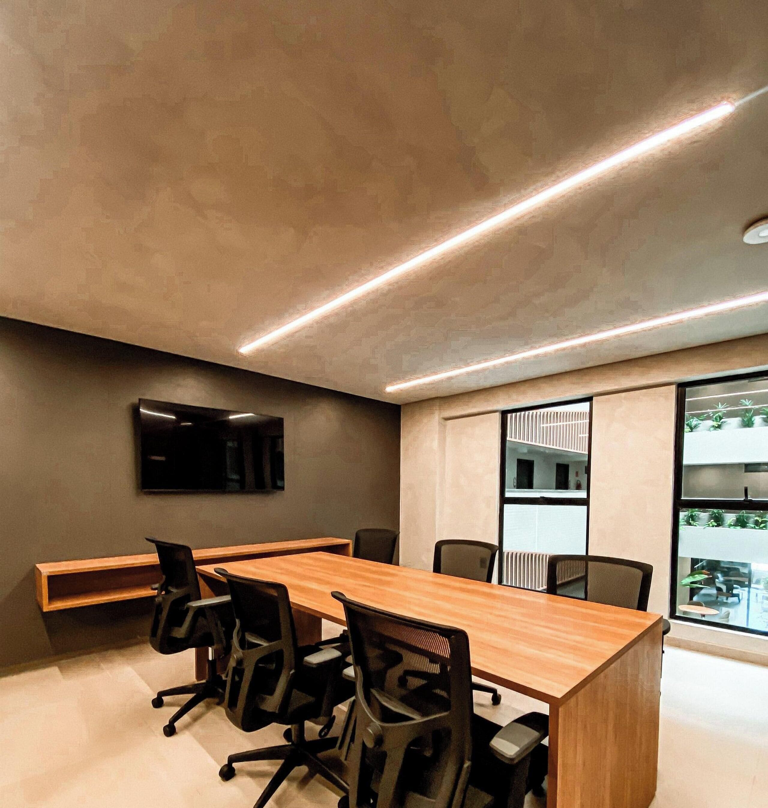Un salón de conferencias con una mesa larga, sillas, un televisor de pantalla plana y una ventana con persianas.