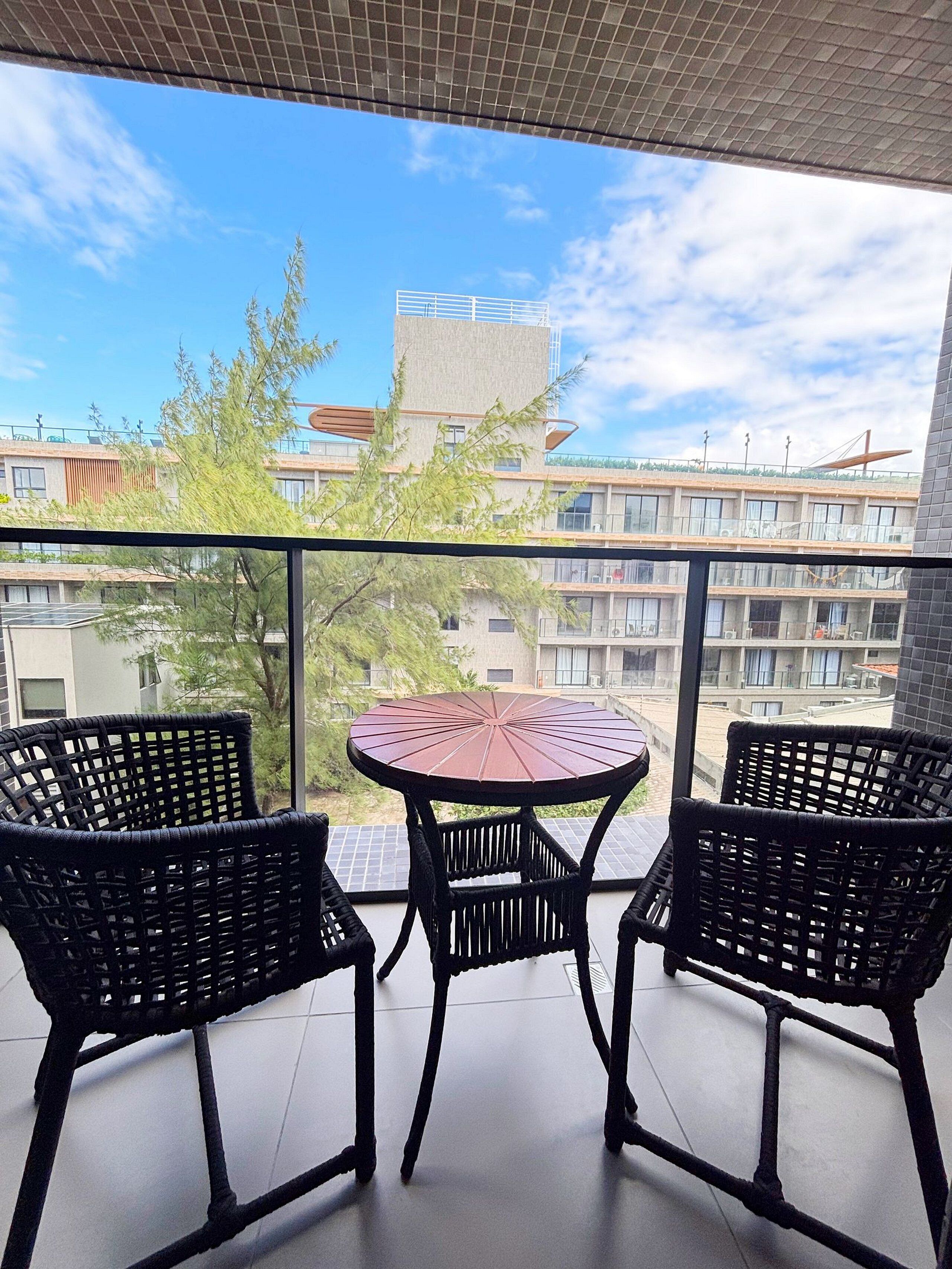 Un balcon avec deux fauteuils en osier et une table ronde, donnant sur un immeuble au design moderne et un ciel dégagé.